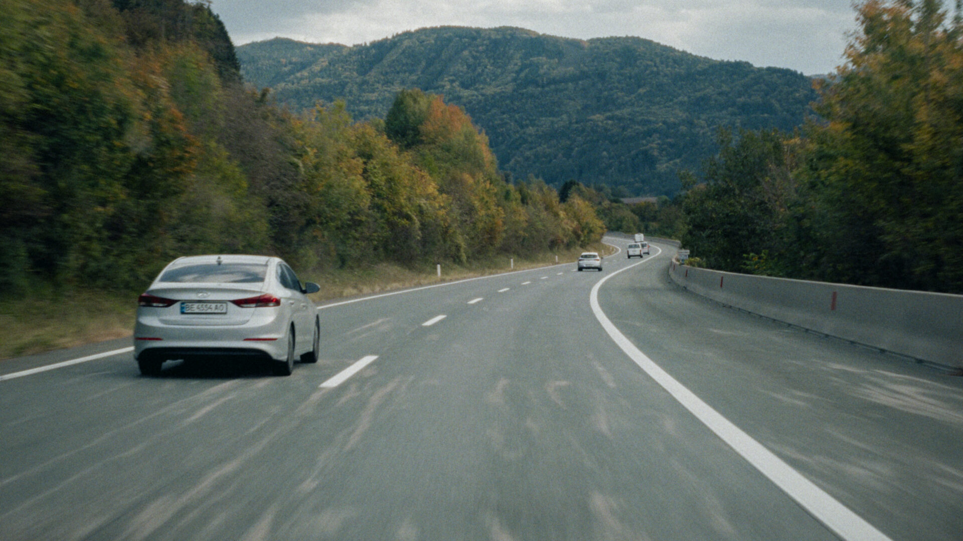 Autobahn mit mehreren Autos durch bewaldete Berge unter bewölktem Himmel
