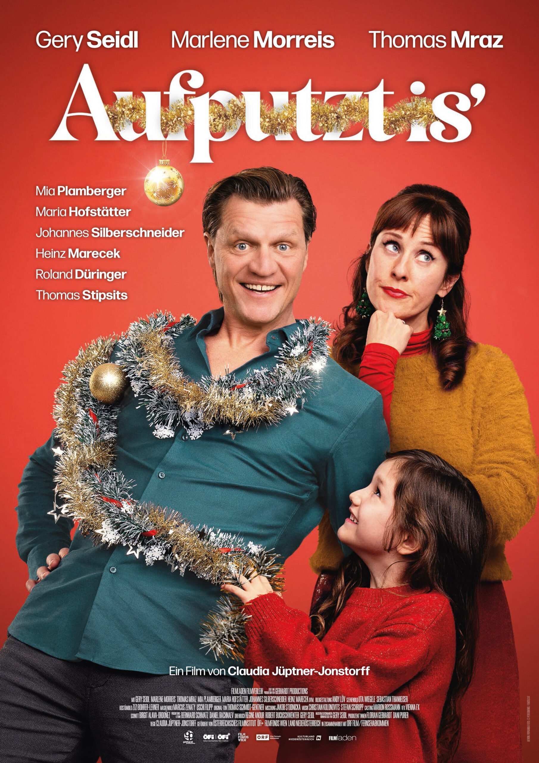 Filmplakat für "Aufputzt is'" mit drei lachenden Personen vor rotem Hintergrund: Ein Mann ist mit Lametta geschmückt, daneben eine Frau mit Weihnachtsohrringen und ein Kind im roten Pullover, das zu ihm aufschaut. Oben sind die Hauptdarsteller und der Filmtitel groß abgebildet.