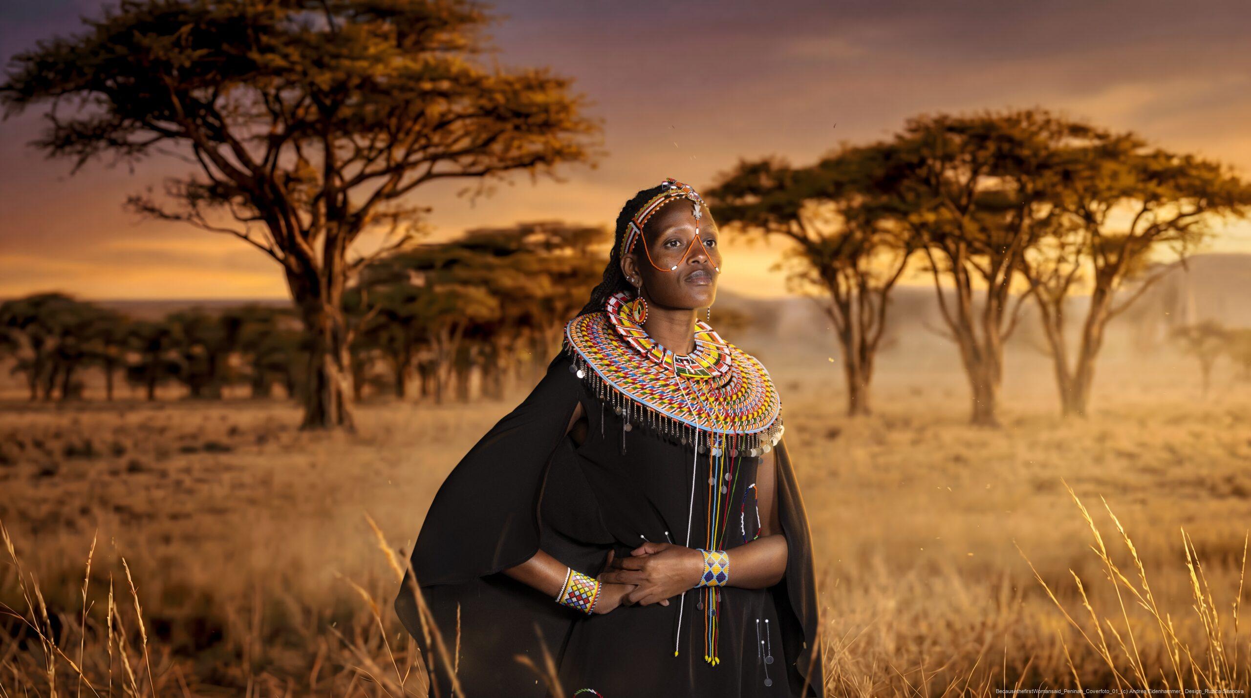 Frau in traditioneller afrikanischer Kleidung und Schmuck steht vor einer Savannenlandschaft mit Akazienbäumen bei Sonnenuntergang.