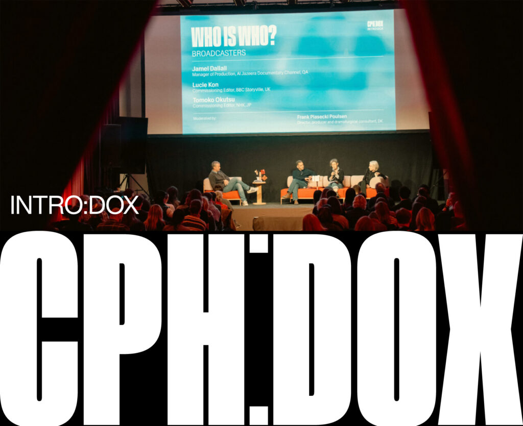 Podiumsdiskussion auf einer Bühne mit vier Personen vor einem Publikum, darüber eine große Leinwand mit Text zu einer Diskussionsrunde bei CPH:DOX; im Vordergrund dominiert die weiße Aufschrift 'CPH:DOX' auf schwarzem Grund.