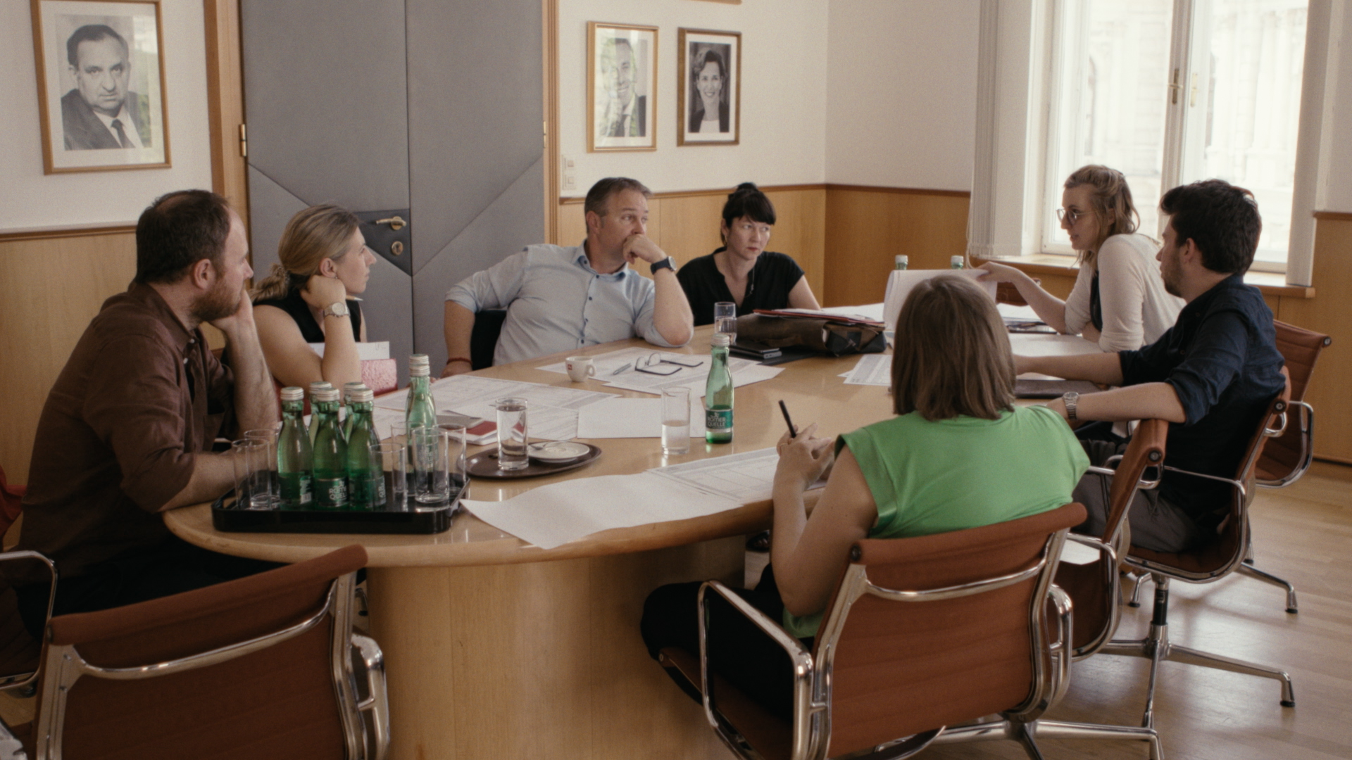 Acht Personen sitzen an einem Besprechungstisch mit Papieren und Wasserflaschen und diskutieren konzentriert. Darunter Andreas Babler.