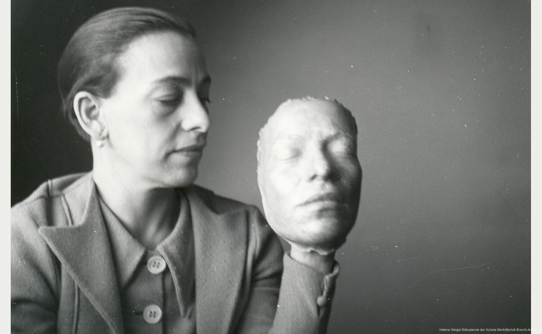Helene Weigel mit Maskenentwurf ca. 1939 im Schwedischen Exil. Eine Frau mit zurückgebundenen Haaren hält eine plastische Gesichtsmaske, die an ein menschliches Gesicht erinnert, in ihrer Hand.