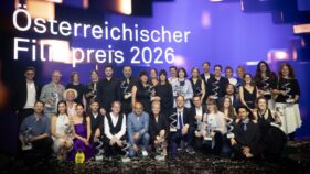 Große Gruppe von Personen mit Trophäen auf einer Bühne vor dem Schriftzug „Österreichischer Filmpreis 2026“.