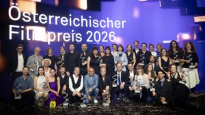 Große Gruppe von Personen mit Trophäen auf einer Bühne vor dem Schriftzug „Österreichischer Filmpreis 2026“.