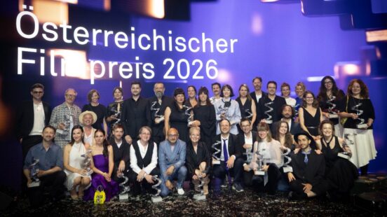 Große Gruppe von Personen mit Trophäen auf einer Bühne vor dem Schriftzug „Österreichischer Filmpreis 2026“.