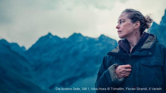 Frau in wetterfester Jacke blickt vor bergigem Hintergrund nach rechts