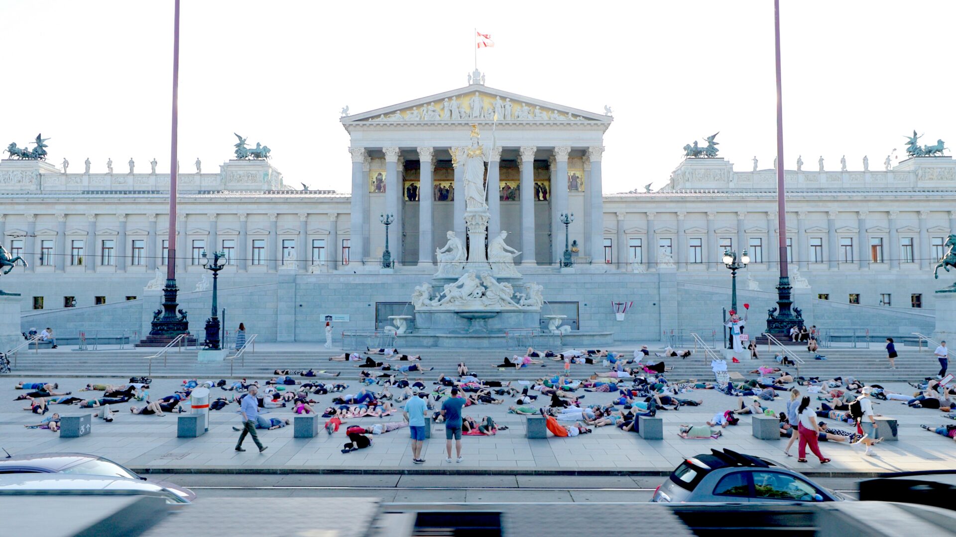 Menschen liegen und sitzen vor dem österreichischen Parlamentsgebäude auf dem Platz