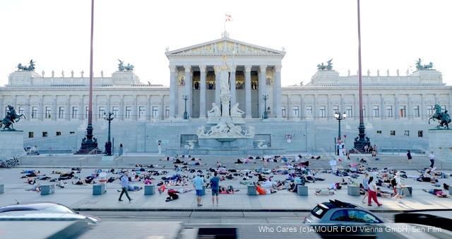 Menschen liegen und sitzen vor dem österreichischen Parlamentsgebäude auf dem Platz