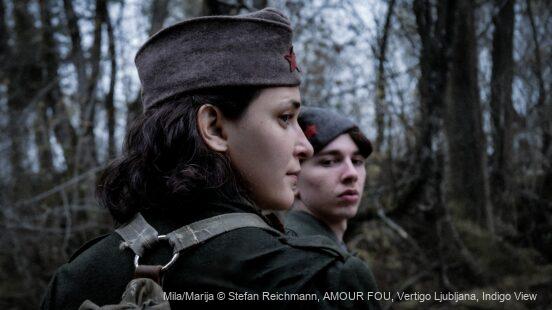 Zwei Personen in historischen Uniformen stehen in einem Wald; die vordere blickt im Profil zur Seite