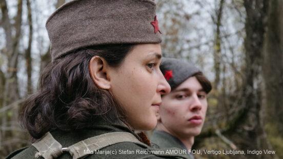 Zwei Menschen in historischer Kleidung und mit roten Sternabzeichen stehen in einem Wald