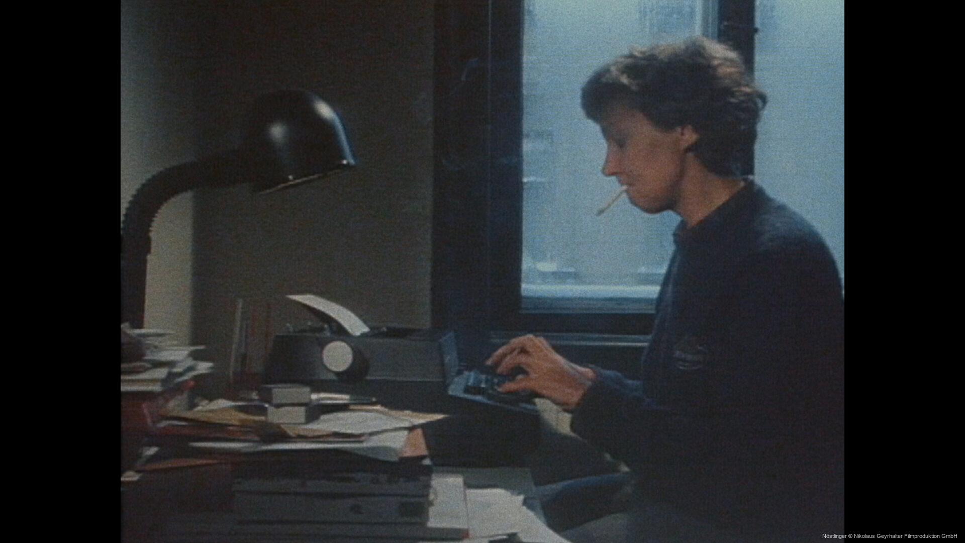 Christine Nöstlinger arbeitet an einem alten Computer an einem Schreibtisch, Zigarette im Mund